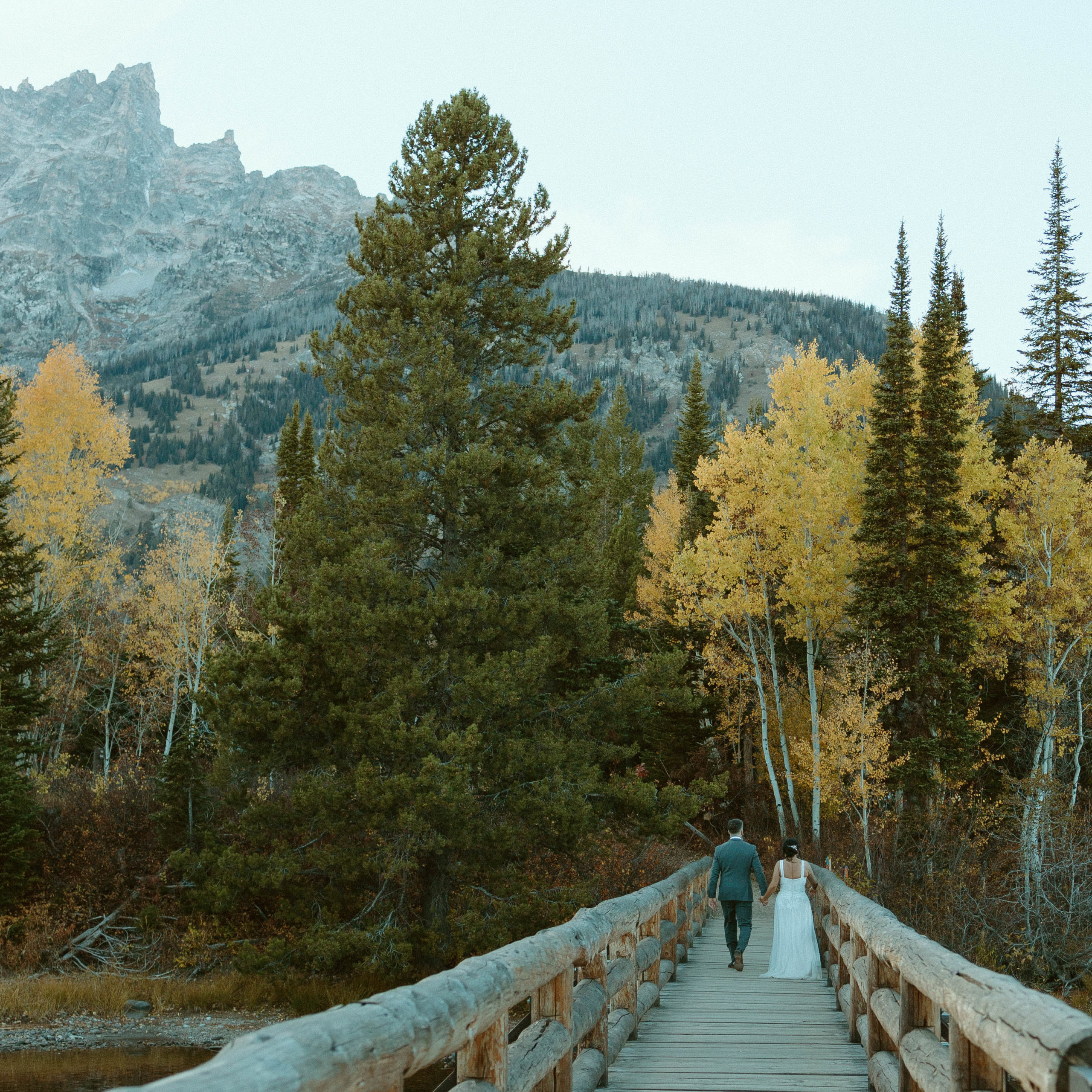couple eloping on a bridge in teton national park with the autumn colors reflecting on Jenny Lake